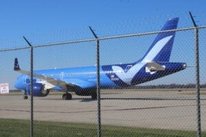A Breeze Airways Airbus A220 sits on the ramp at Abraham Lincoln Capital Airport in Springfield, Illinois, seen through the airfield perimeter fence.