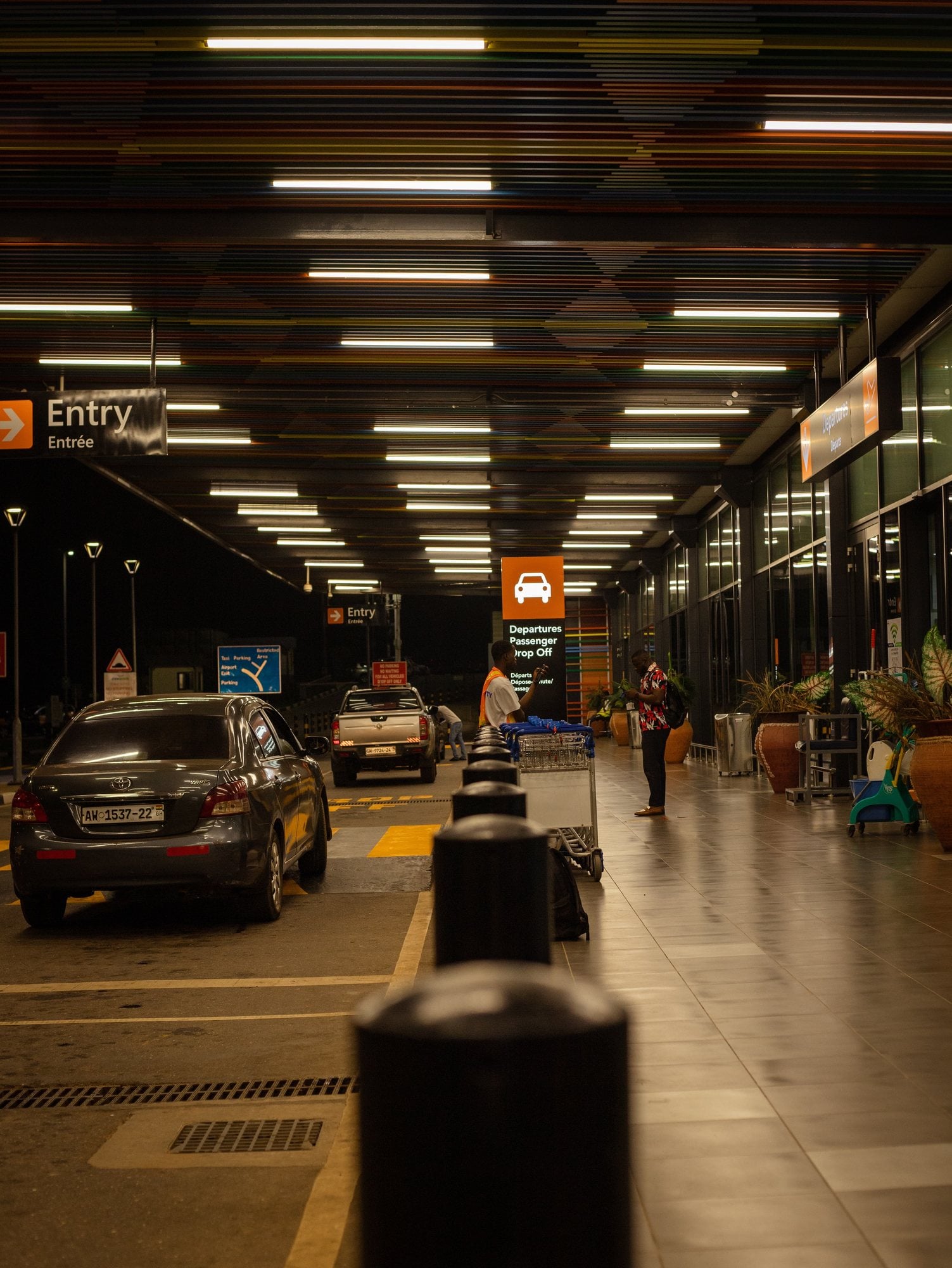 Dark cars stopped at a covered airport departures drop-off lane at night