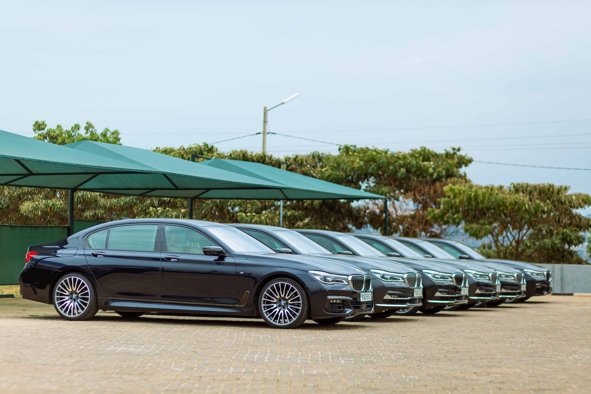 A row of black BMW 7 Series sedans parked side by side under shade canopies.