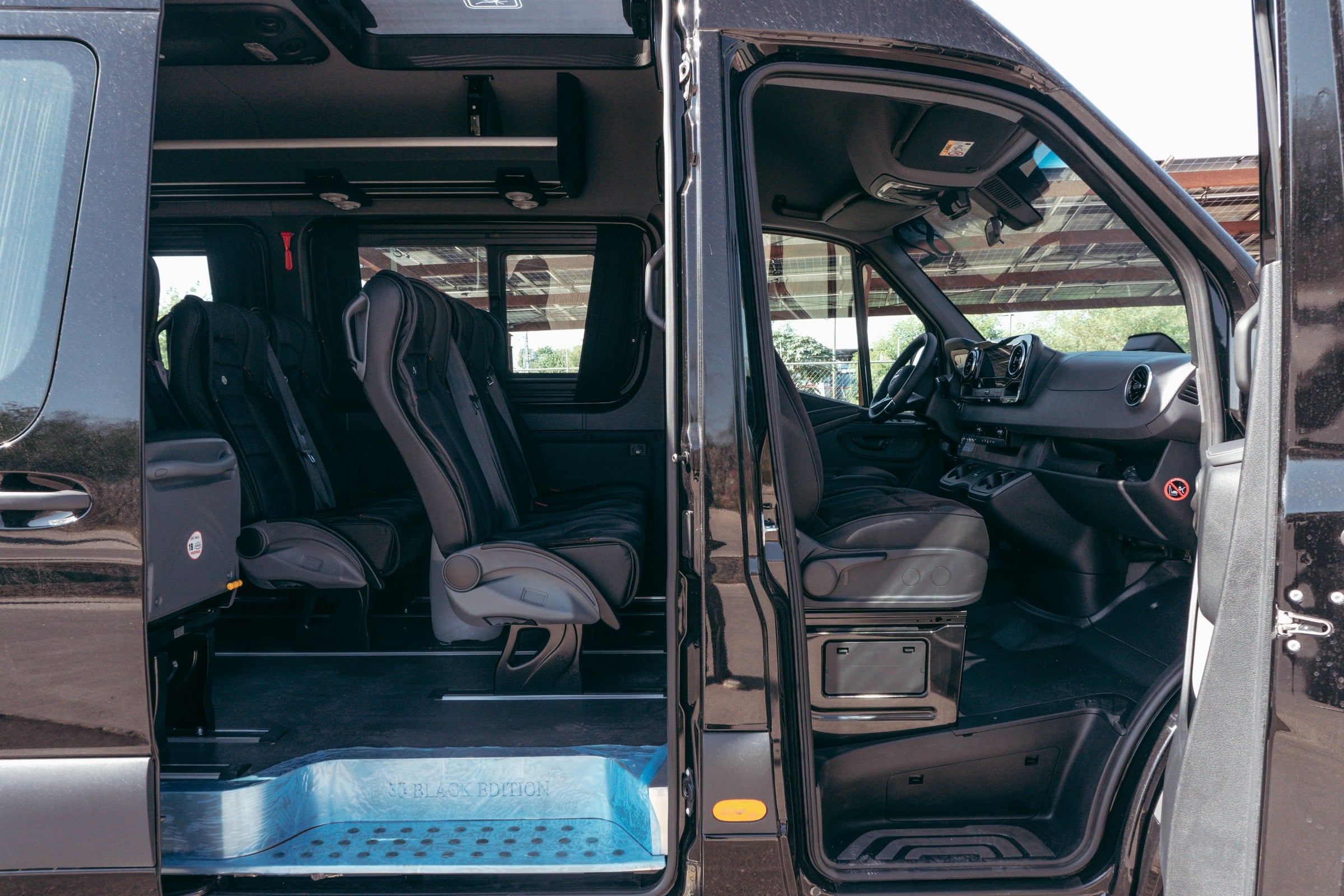 Interior of a black luxury passenger van with black leather seating and open sliding door