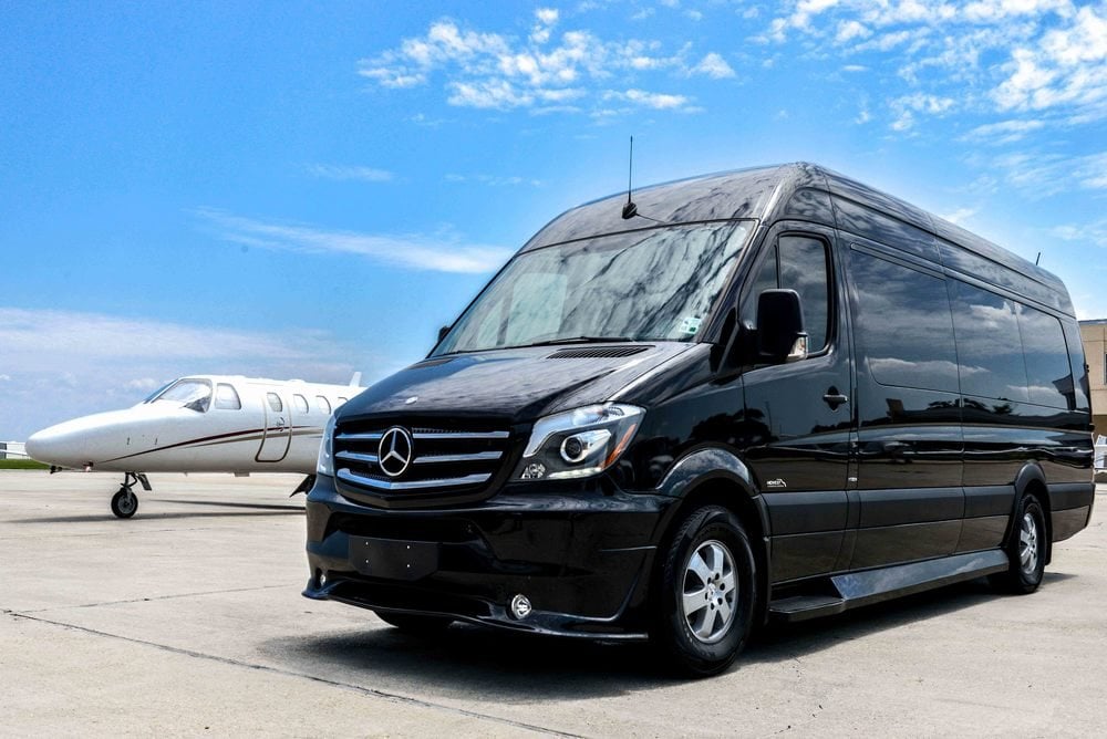 Black Mercedes-Benz Sprinter van parked beside a private jet on the tarmac