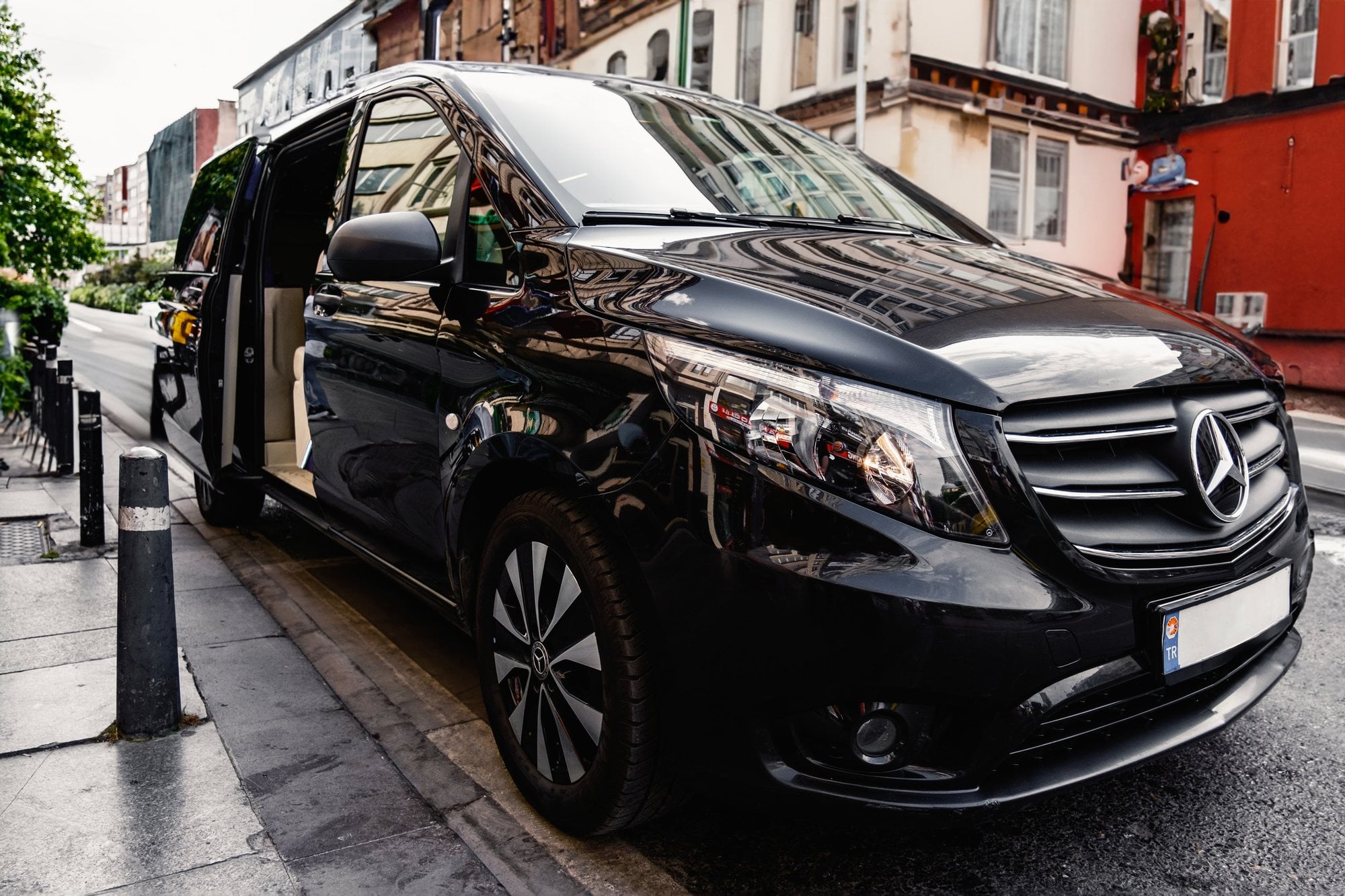 A black Mercedes-Benz passenger van waits outside a venue with its side door open.