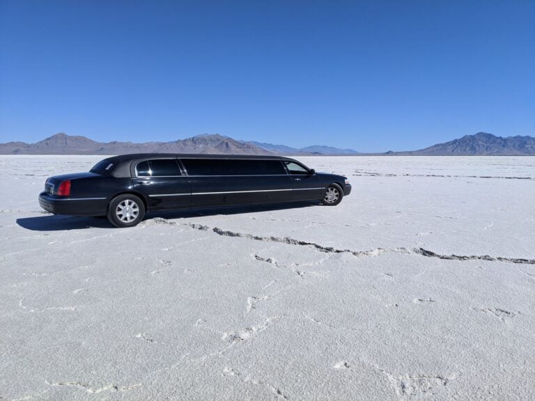 A black stretch limousine parked on a white salt flat under a clear blue sky.