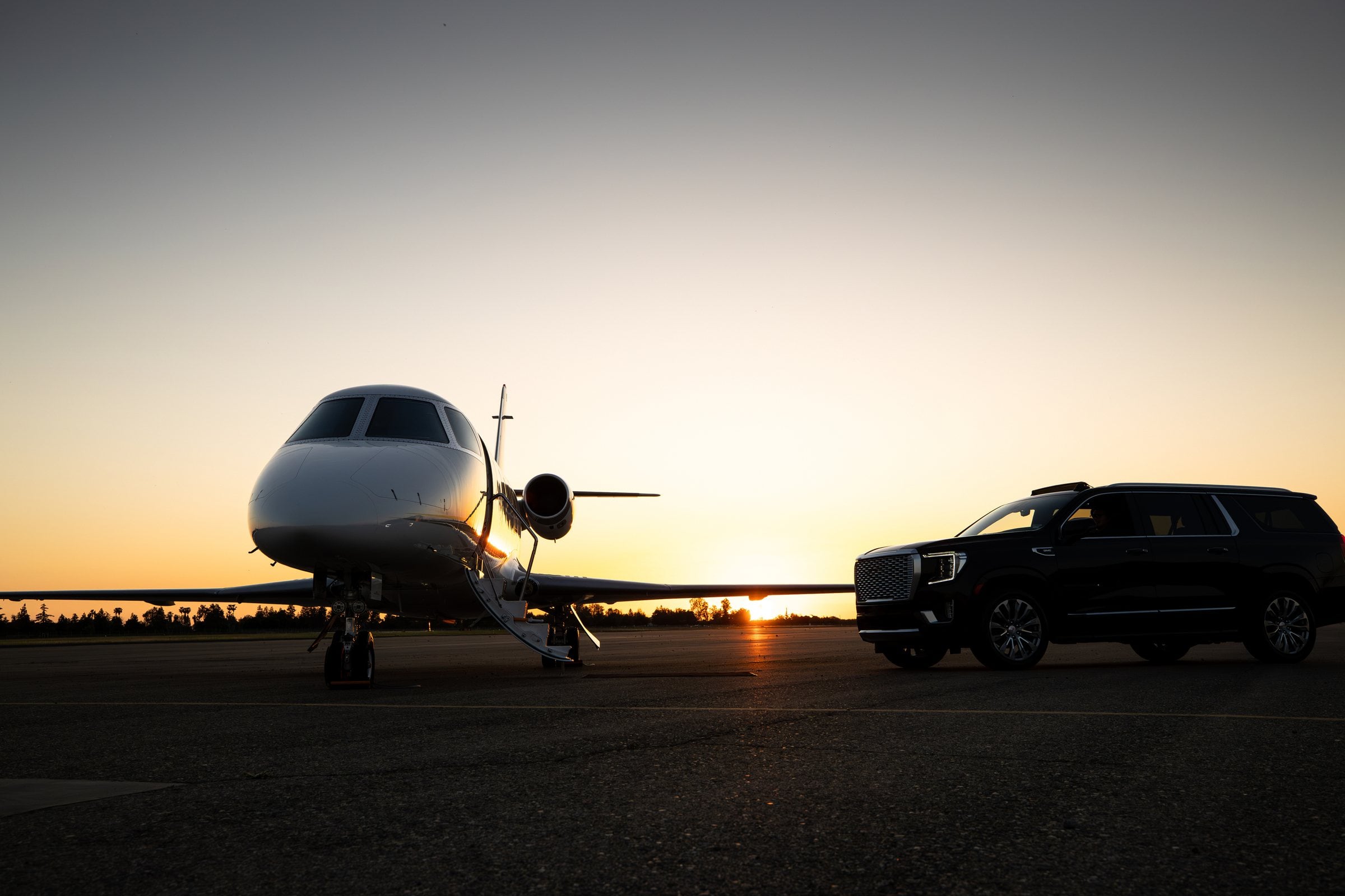 Black SUV waiting beside a private jet at dusk