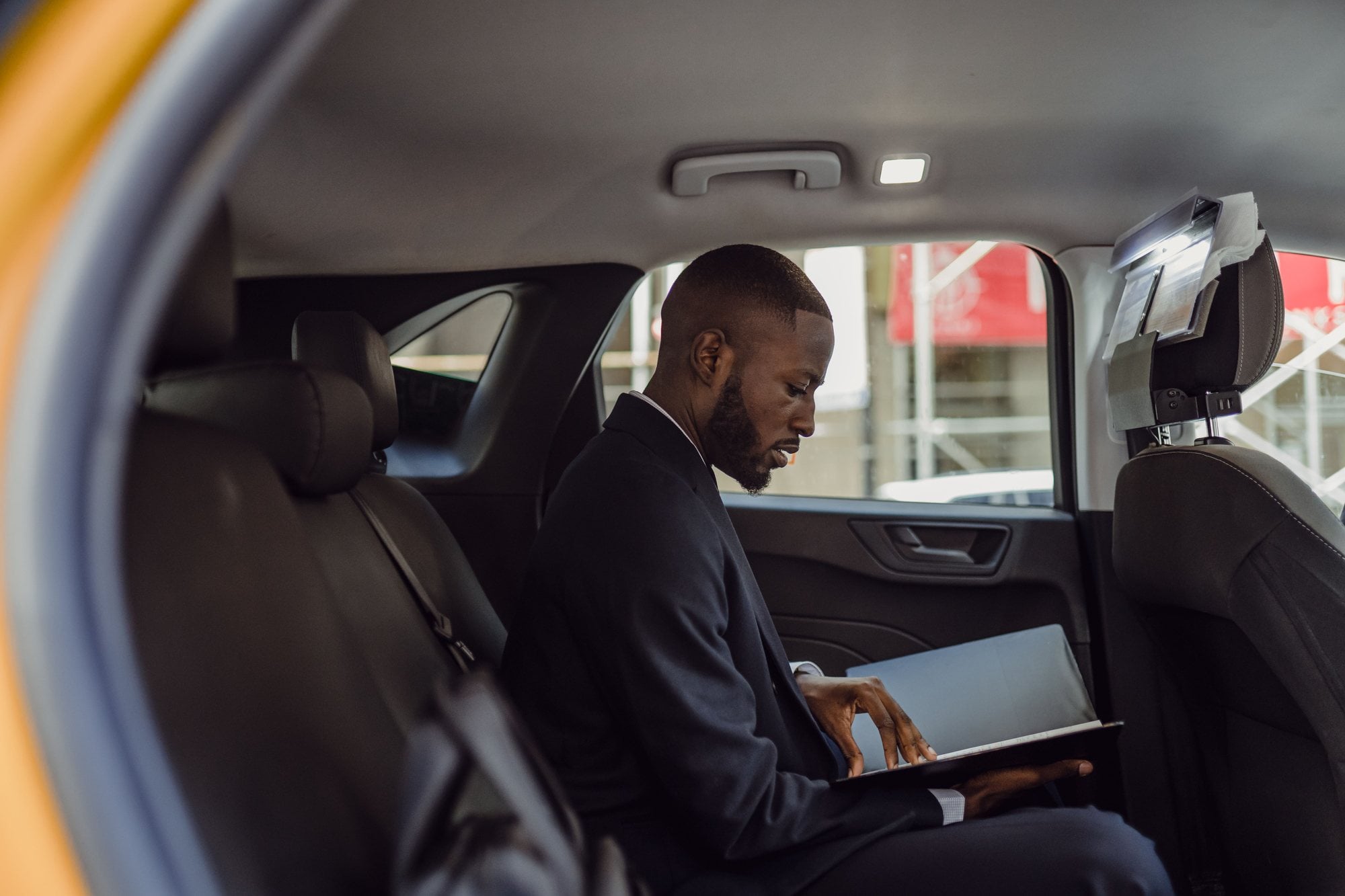 A business traveler in a dark suit reviews documents in the back seat of a car.