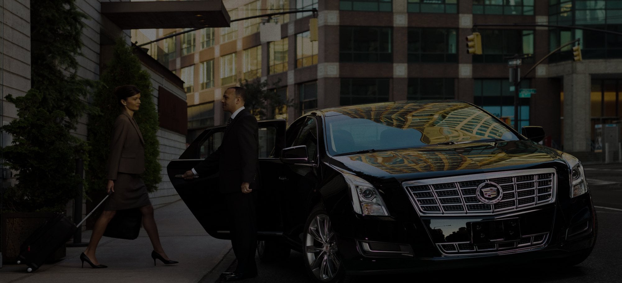 Chauffeur holding the door of a black Cadillac for an arriving traveler