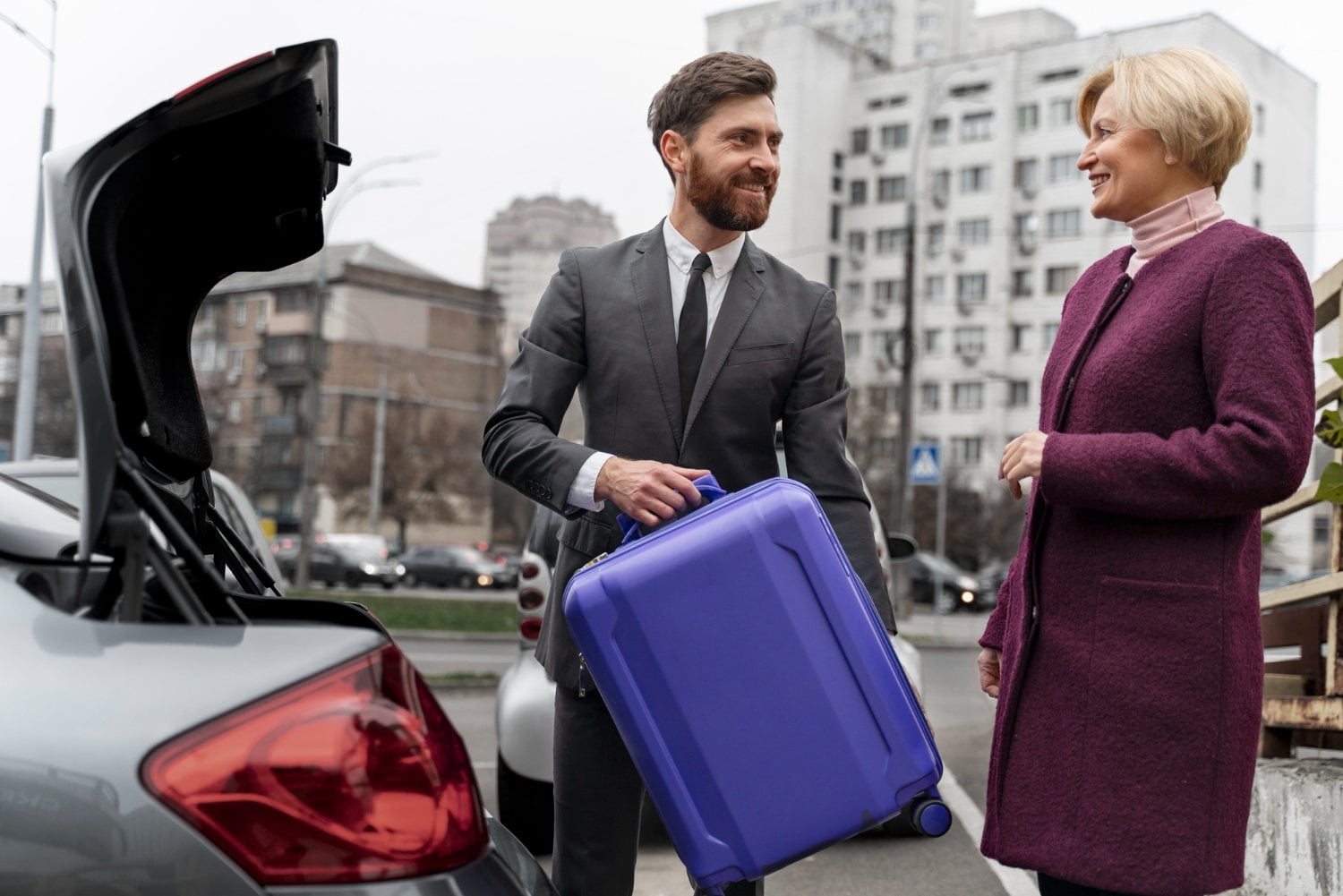 Chauffeur in a suit greeting a traveler with a suitcase beside a car