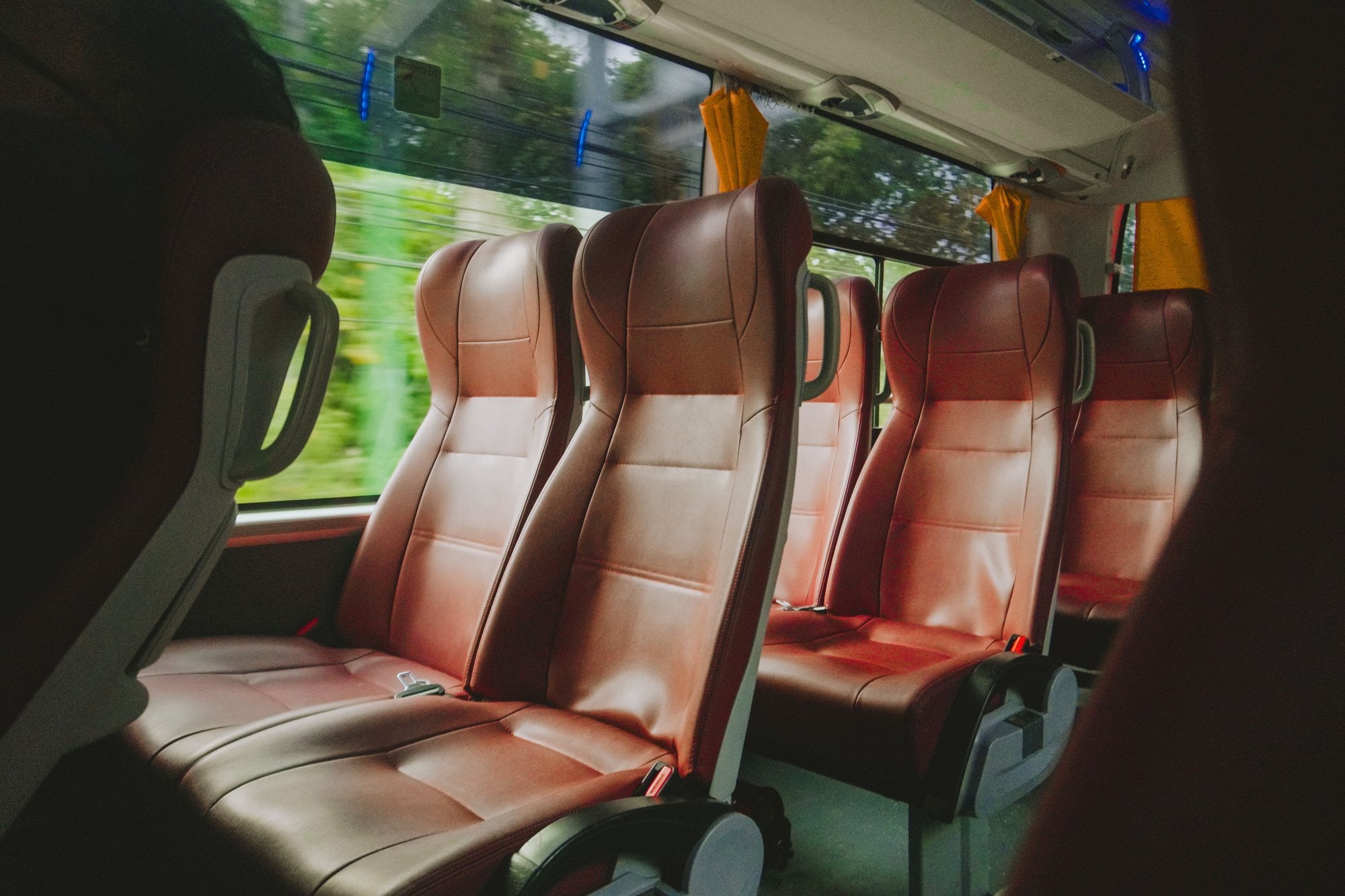 Rows of empty reclining leather seats line the interior of a moving passenger coach.