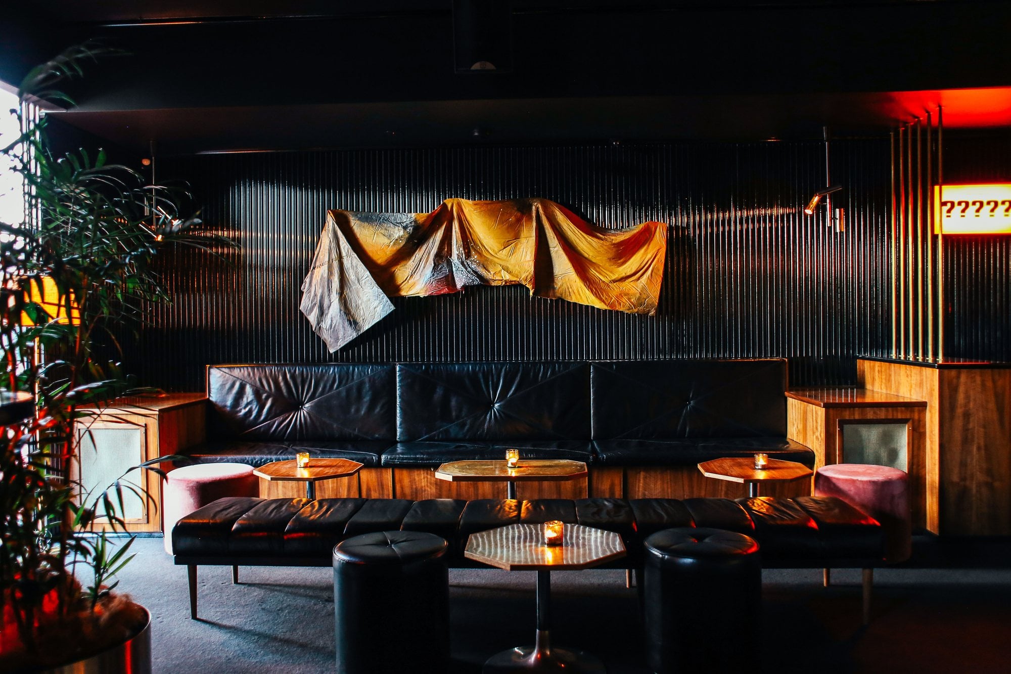 Black leather banquettes and candlelit brass tables fill the dark interior of an upscale restaurant.