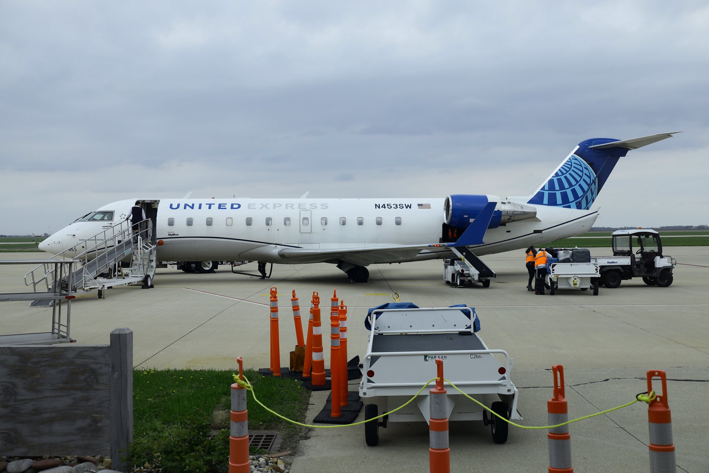 A United Express Bombardier CRJ200 with its airstair down on the ramp at Decatur Airport in Illinois while ground crew load baggage