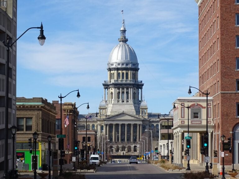 A downtown Springfield street lined with brick storefronts leads toward the silver dome of the Illinois State Capitol.