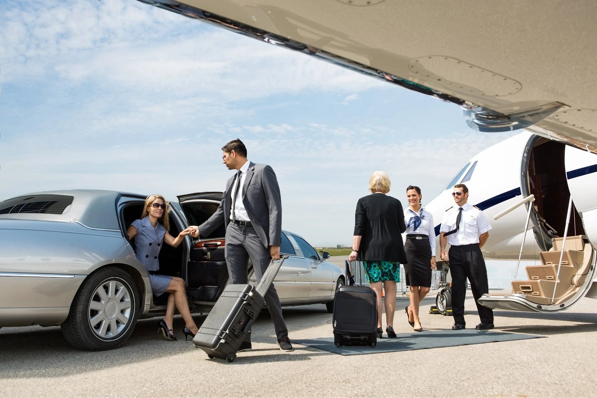 Chauffeur helping passengers beside a stretch limousine and a private jet