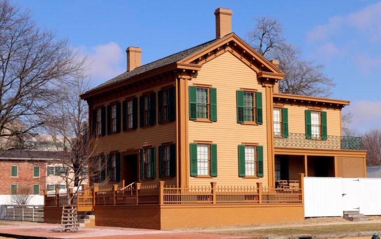 The tan and green Lincoln Home National Historic Site stands behind its wooden fence under a blue sky in Springfield, Illinois.