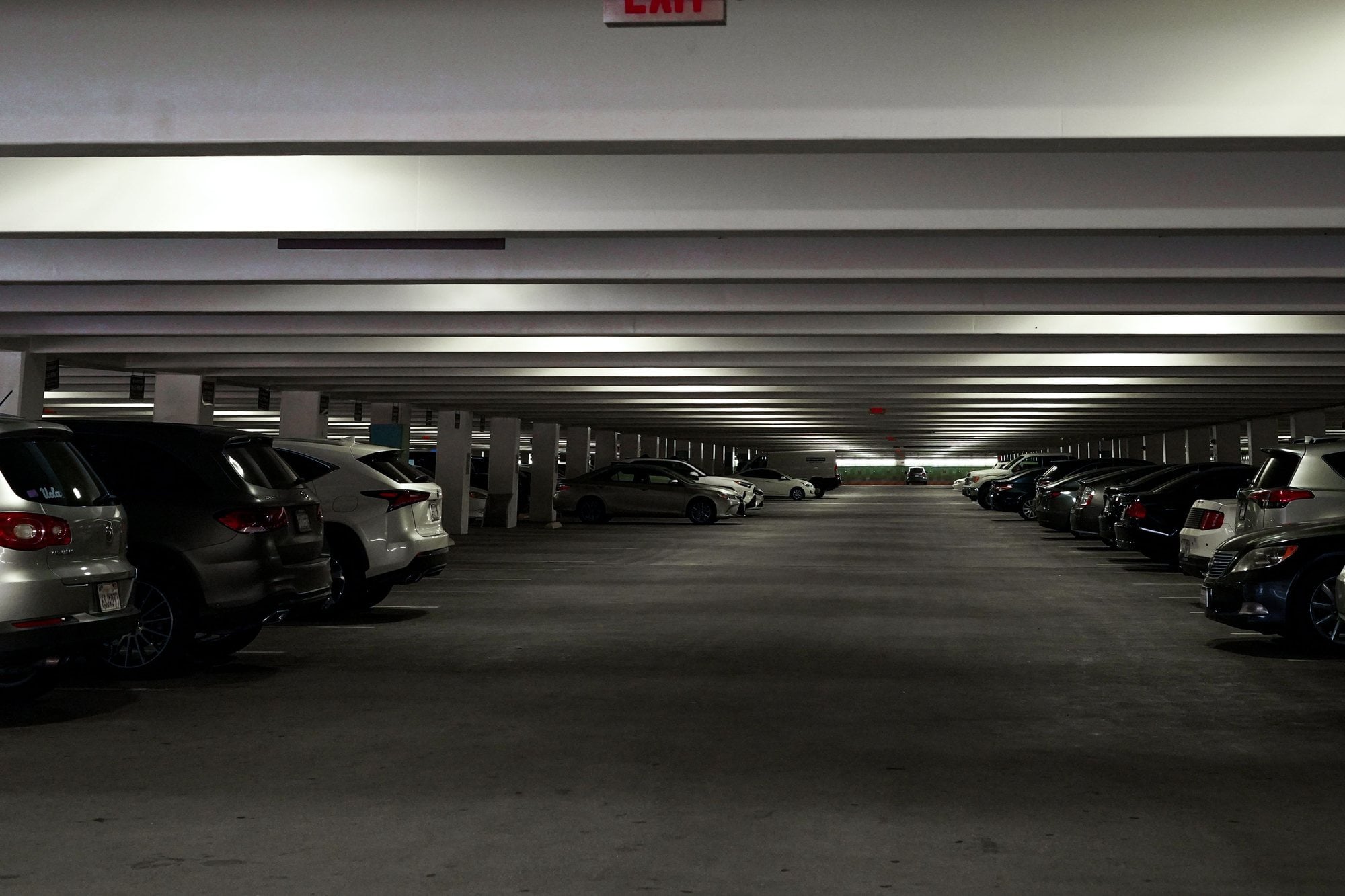 Rows of parked cars fill a dim level of a multi-story parking garage.