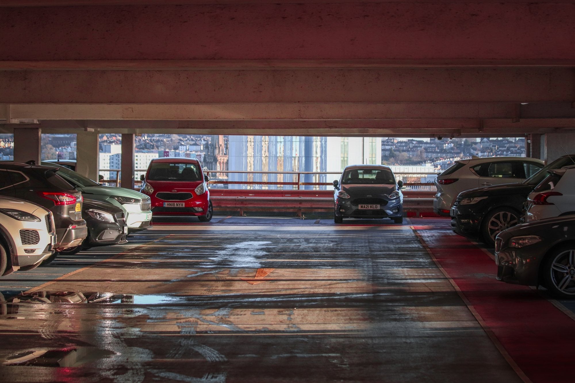 Rows of parked cars on an upper deck of a multi-level parking garage with a city skyline beyond