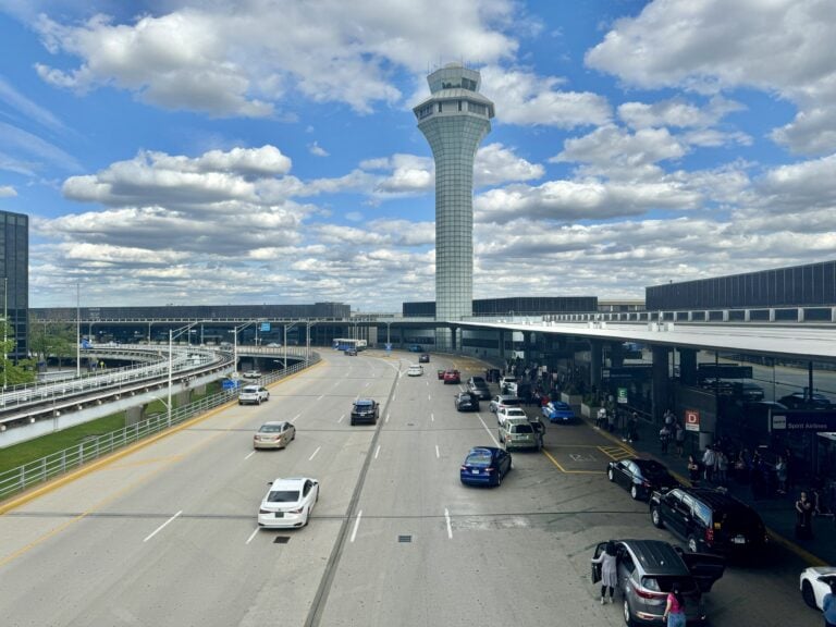 Cars and taxis line the roadway in front of Terminals 2 and 3 at Chicago O'Hare International Airport beneath the control tower.