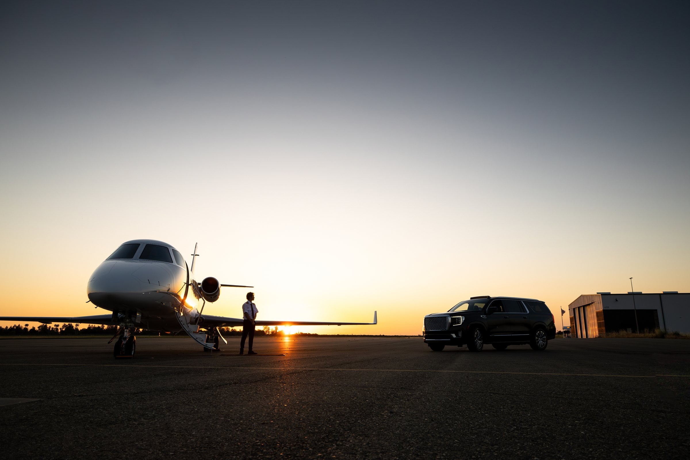 Private jet with its stairs down beside a black SUV at sunset