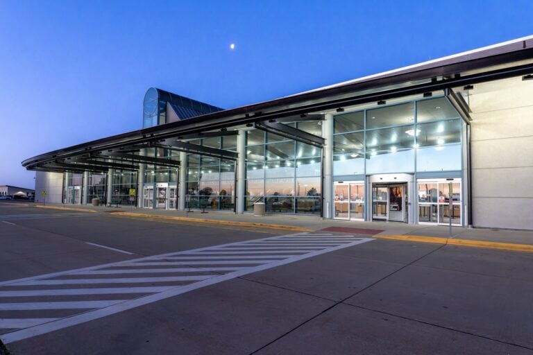 The lit glass terminal building at University of Illinois Willard Airport at dusk with an empty departures roadway.